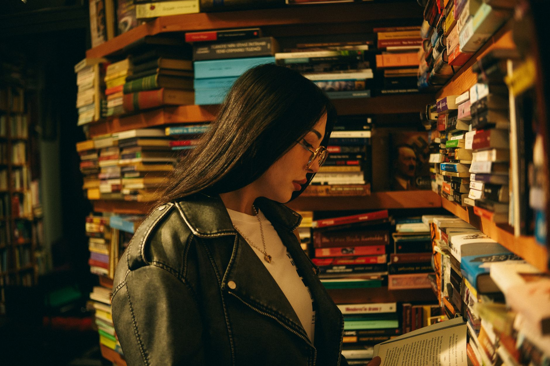 A woman engrossed in reading amidst a cozy bookstore with stacked shelves.