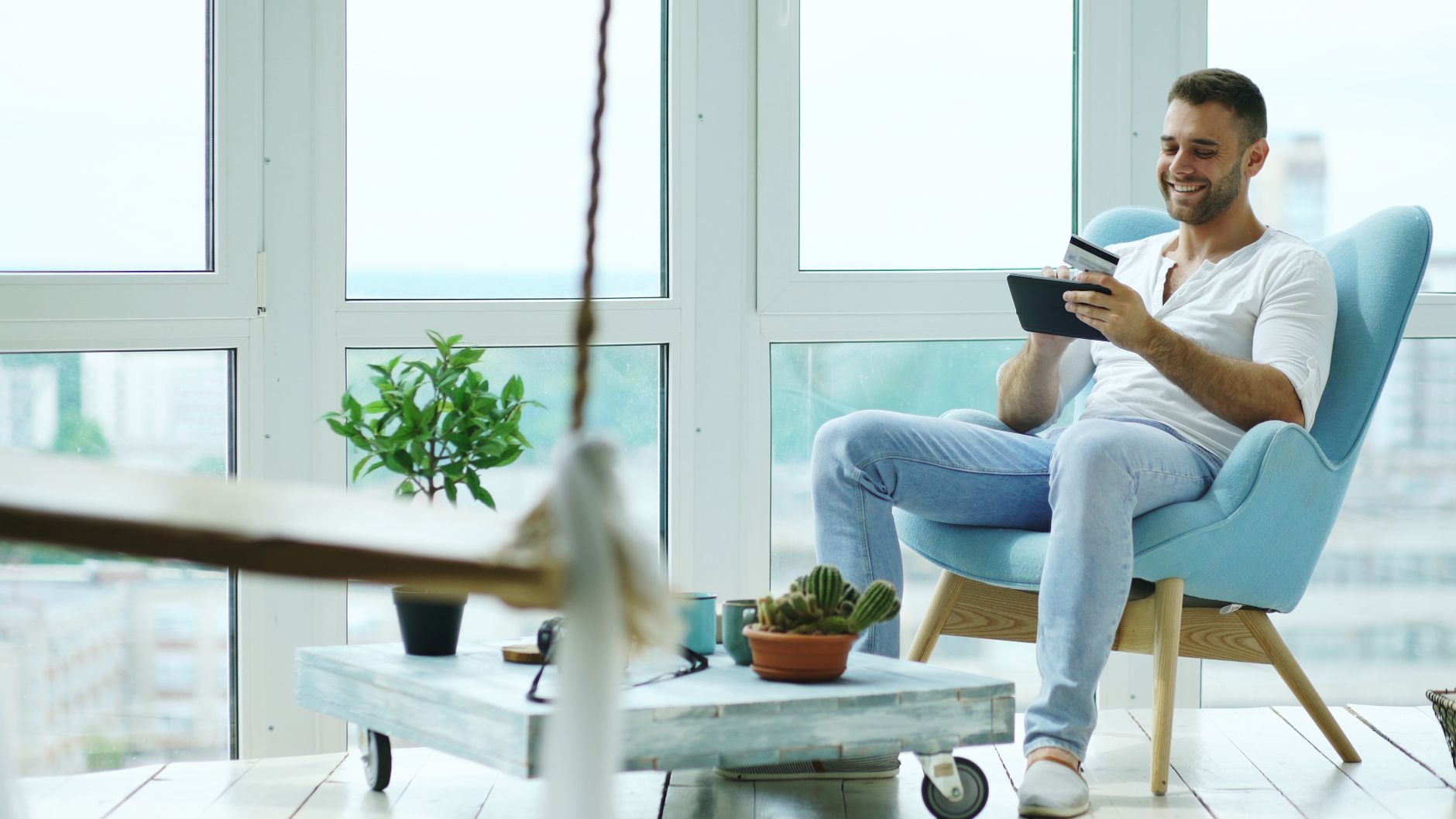 Relaxed man using tablet in a bright, modern living room with plants.