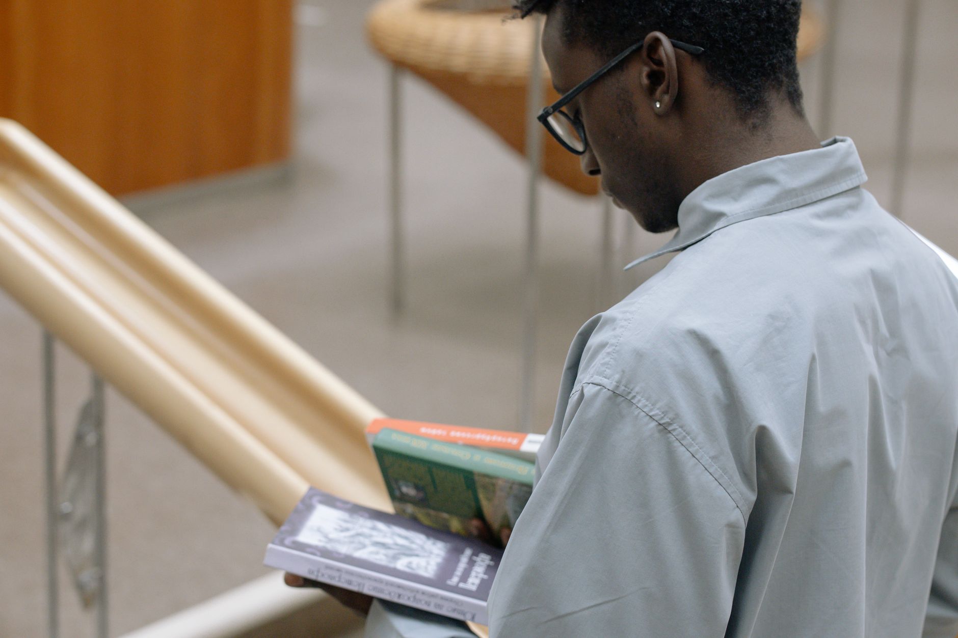 Back view of a man reading books in a library, promoting learning and literature.
