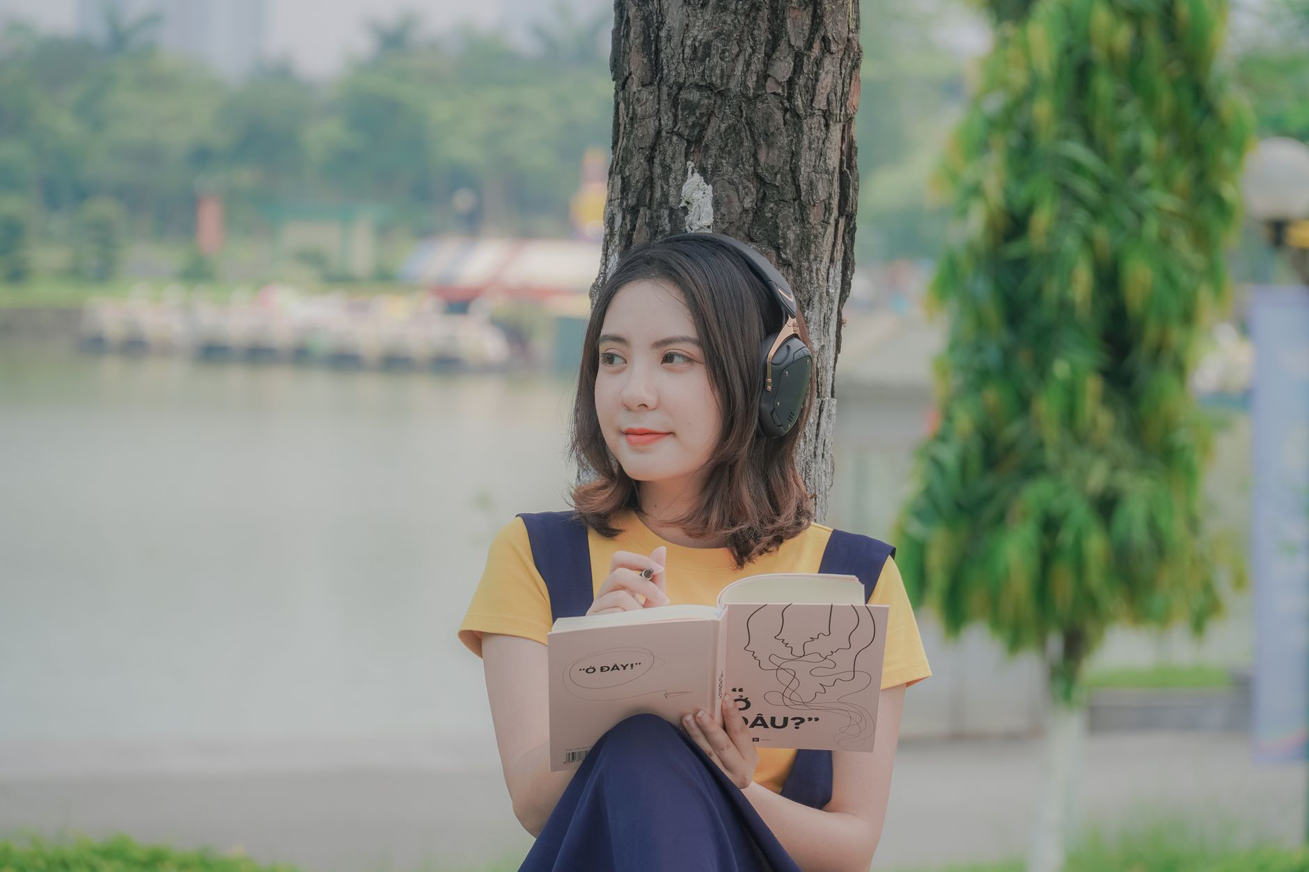 Woman listens through headphones while reading a book outdoors.